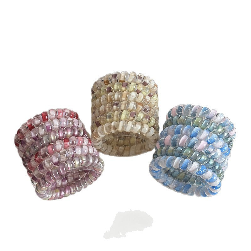 Three coiled multicolor high-stretch hair ties in pink, neutral, and blue designs