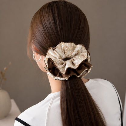 Large cream and brown floral fabric scrunchie with ruffled layers and pearl accents worn in a ponytail