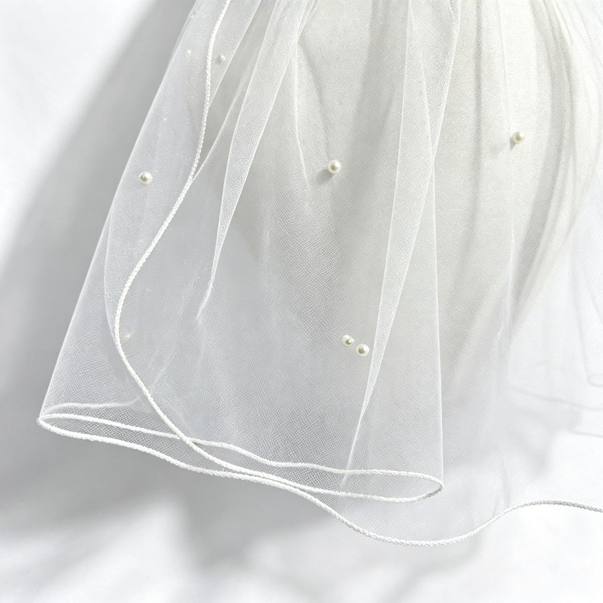 Close-up of sheer veil fabric, faux pearls, and finished edge